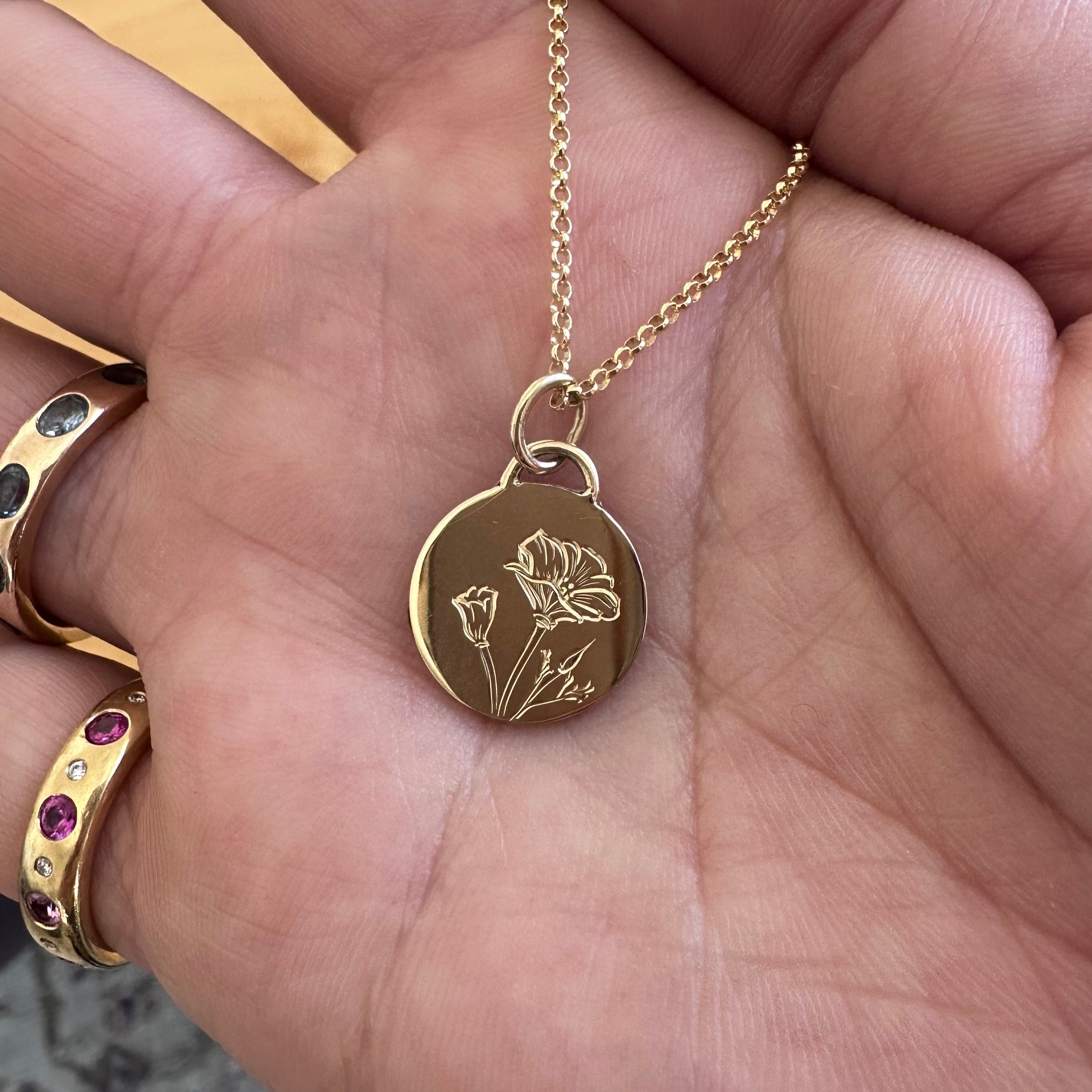 14k Yellow Gold necklace with a hand engraved flower motif on a pendant held in a hand