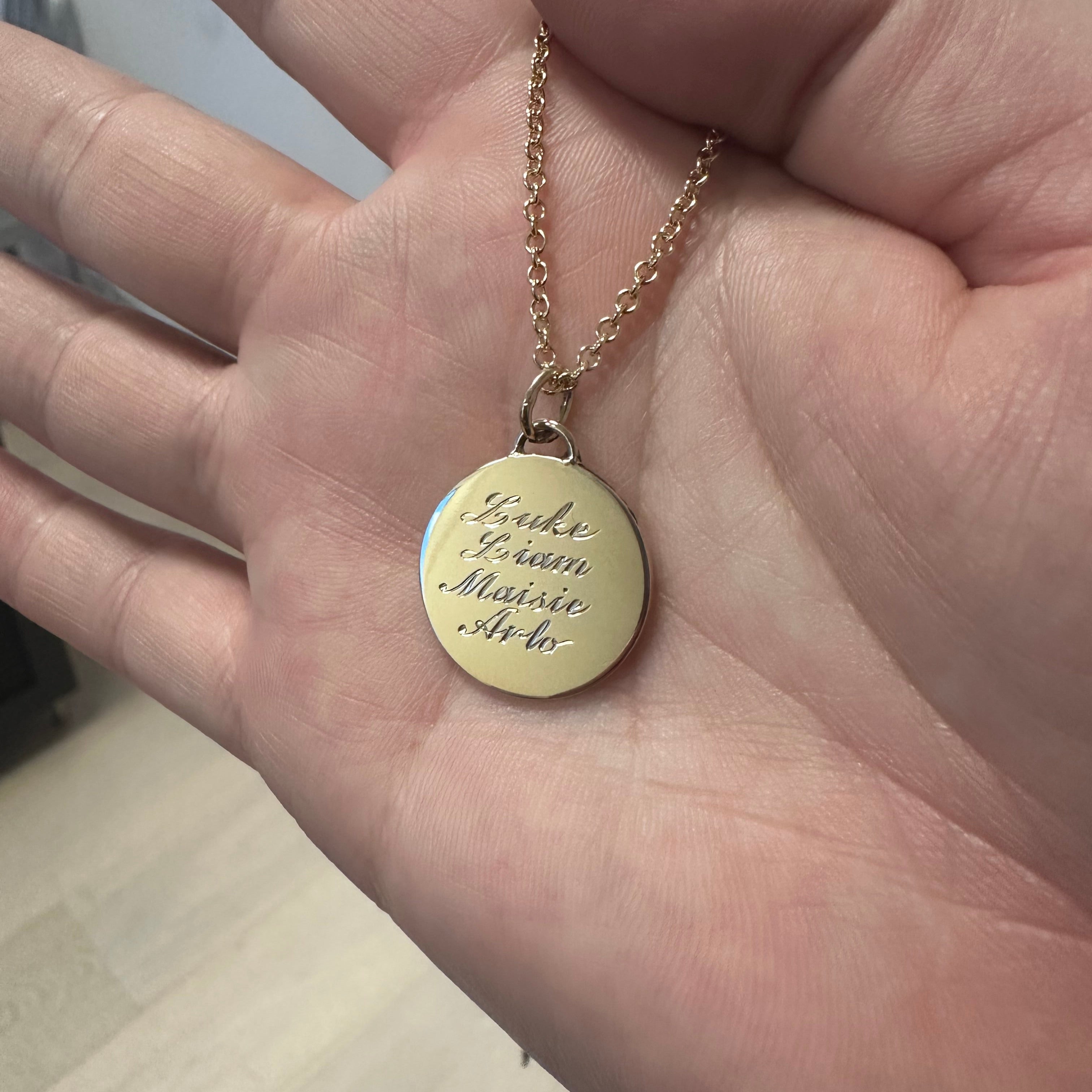 14k Yellow Gold necklace with a round pendant and chain held in a hand